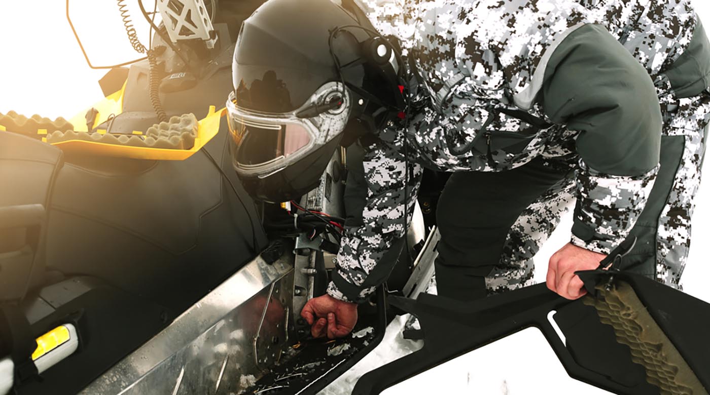 driver repairing broken snowmobile