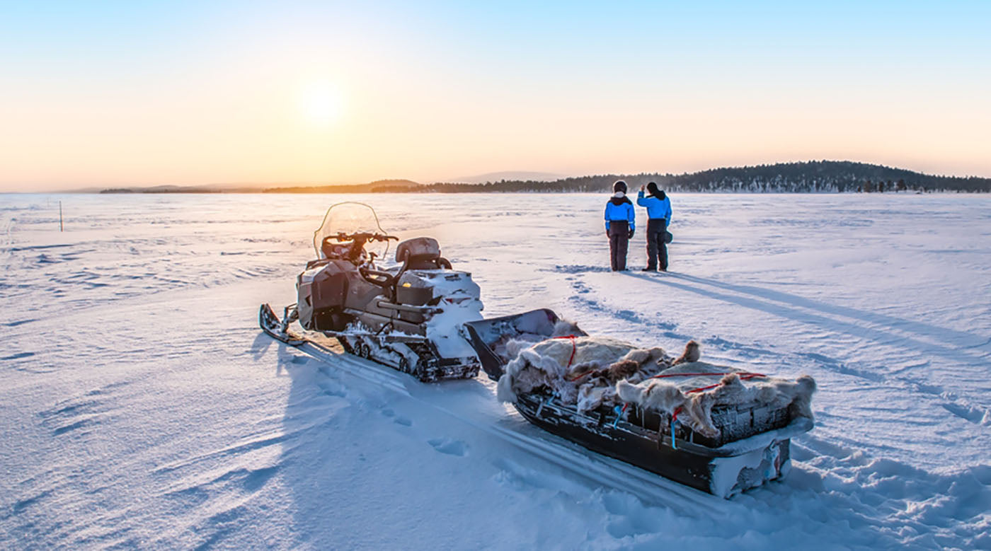 couple enjoy sunrise near snowmobile