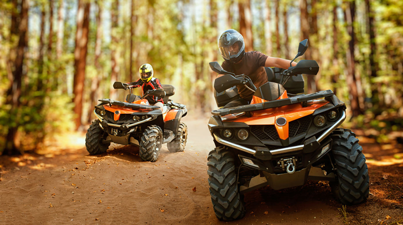 two atv riders speed down forest road
