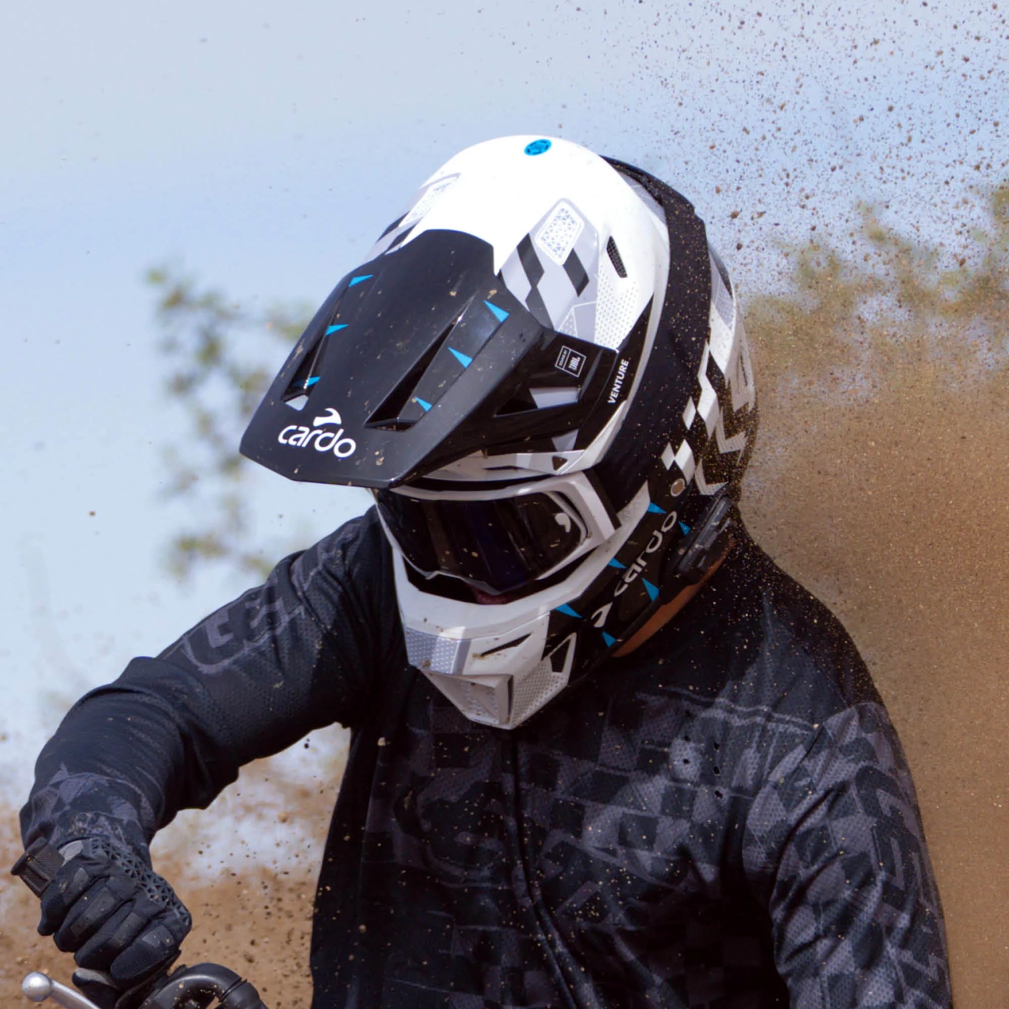 Cardo Venture off-road motorcycle helmet, lifestyle action shot of rider through dust spray