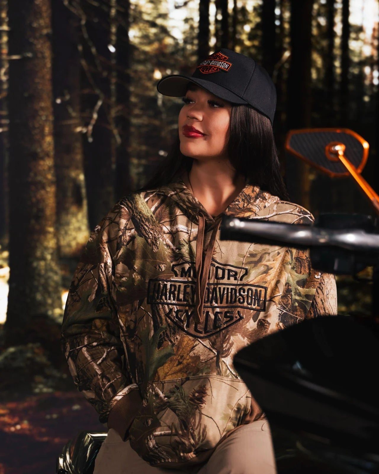 Mar Orts standing beside her motorcycle in a wooded setting.