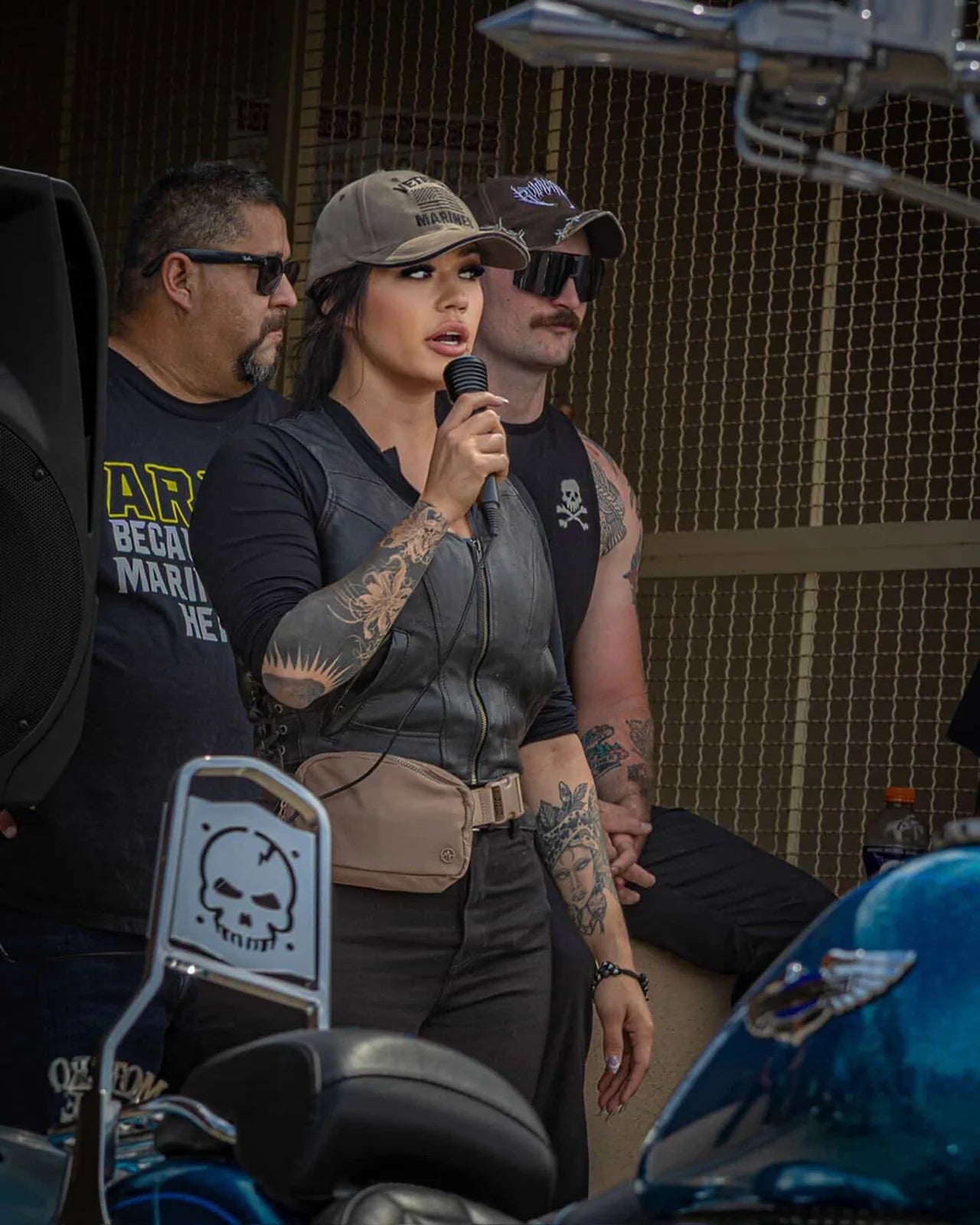 Mar Orts speaking into a microphone at a motorcycle community event.
