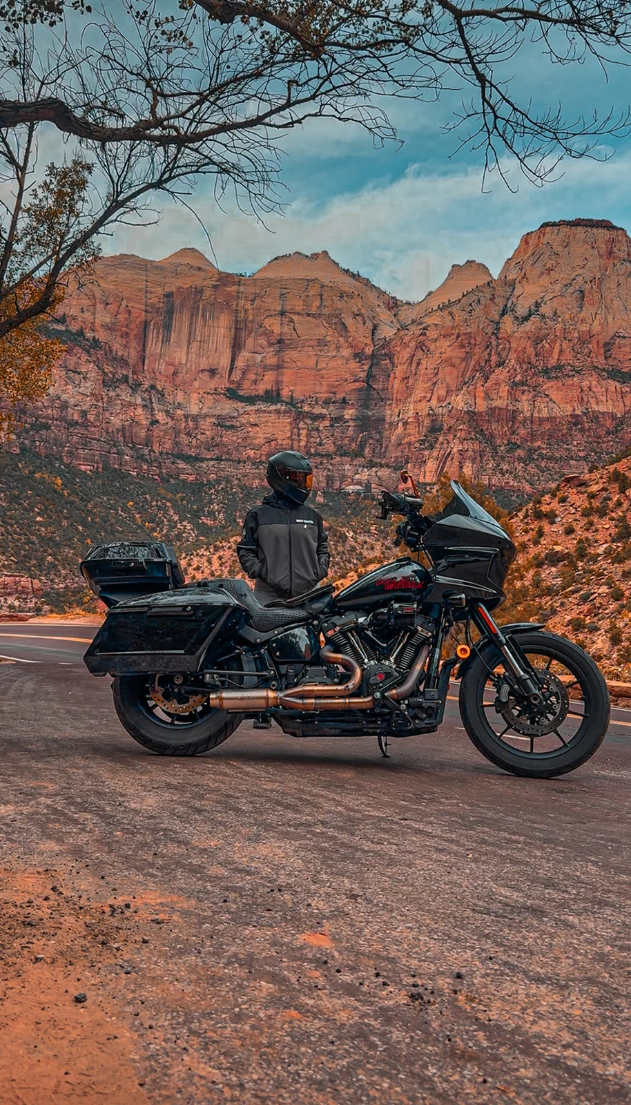 A rider and touring motorcycle beneath the red cliffs of Zion National Park.